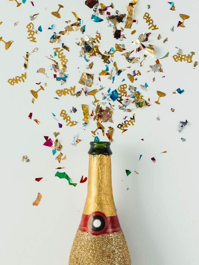 Champagne bottle with cork popping and colourful confetti flying upwards.