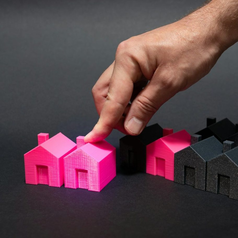 Image of a hand over coloured model houses with 3 pink and the remainder black